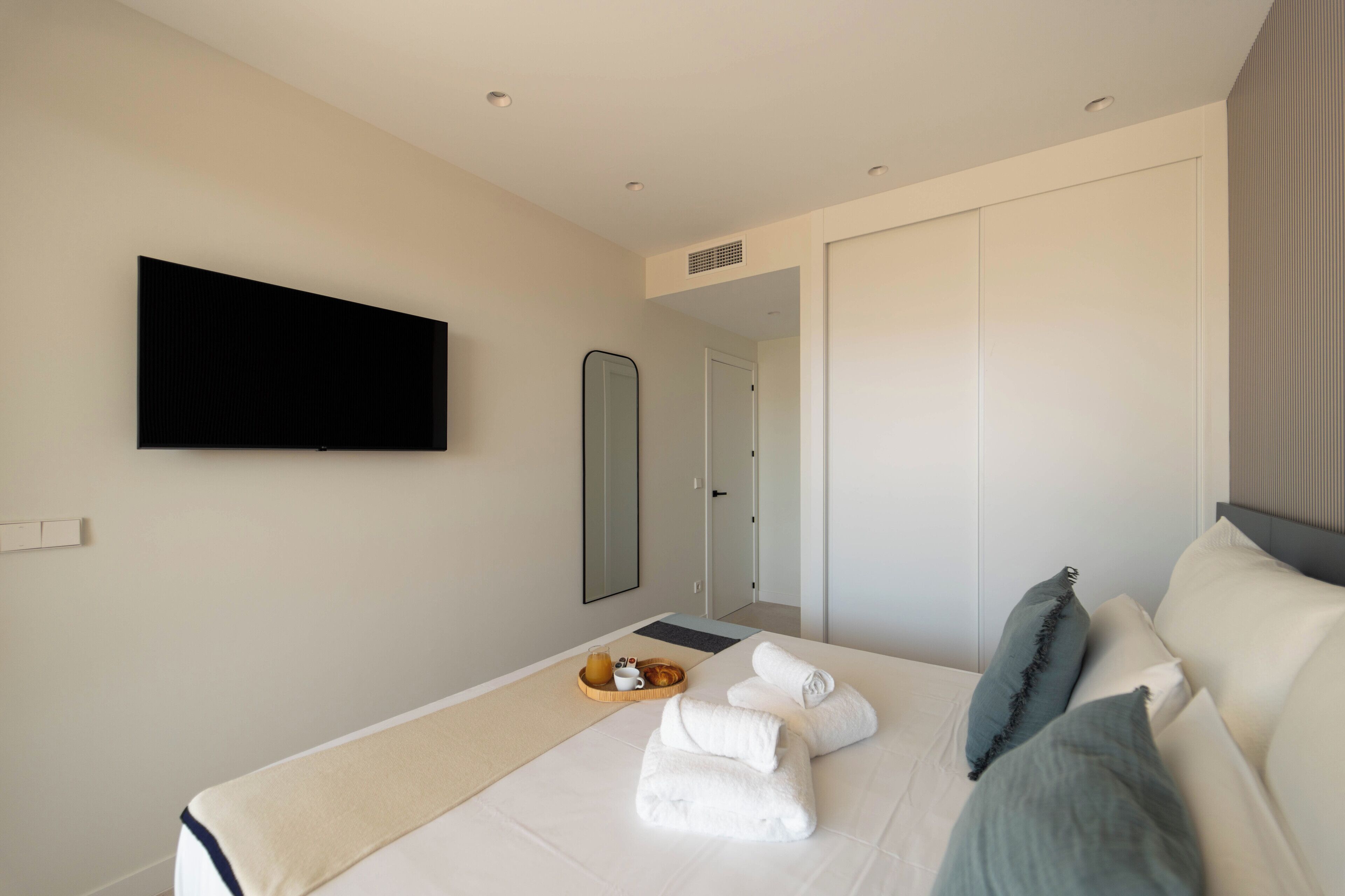Habitación de hotel con cama, televisor de pantalla plana montado en la pared, espejo y puerta que da a otra habitación.