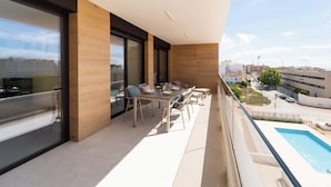 A balcony with a dining table and chairs, large windows, and a view of a swimming pool and buildings. - Lucentina Line (Villajoyosa)