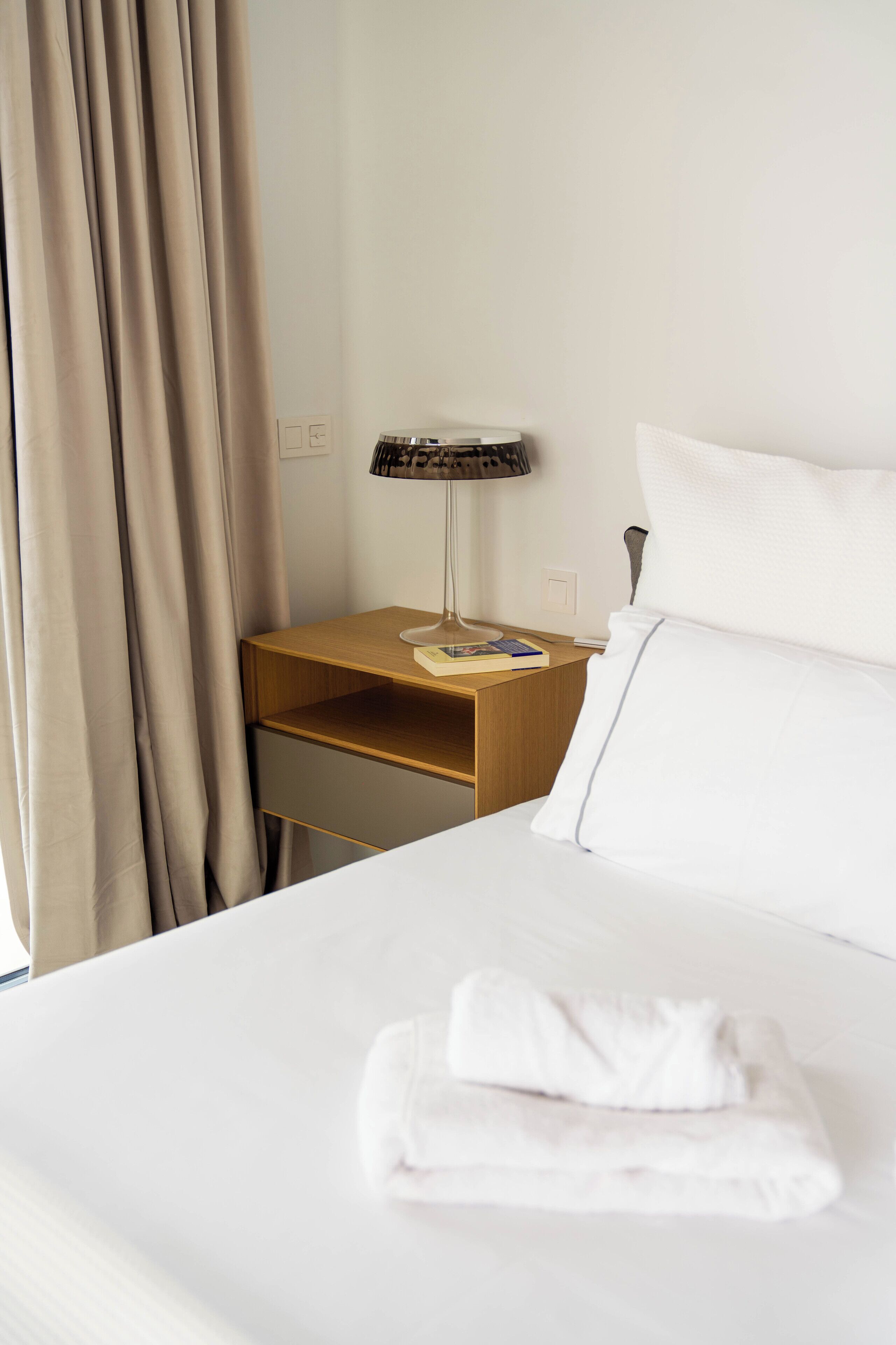 Un lit bien fait, avec une serviette pliée, une table de chevet avec une lampe et une petite table de nuit.