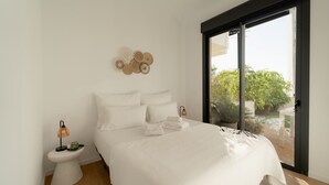 A modern bedroom with a large bed, a bedside table with a lamp, and a view of the outdoors through a sliding door. - Lucentina Line (Villajoyosa)