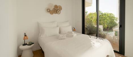 Un dormitorio moderno con una cama grande, una mesita de noche con lámpara y vistas al exterior a través de una puerta corrediza.