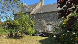 A stone building with a sloped roof, a chimney, and a window with shutters.
