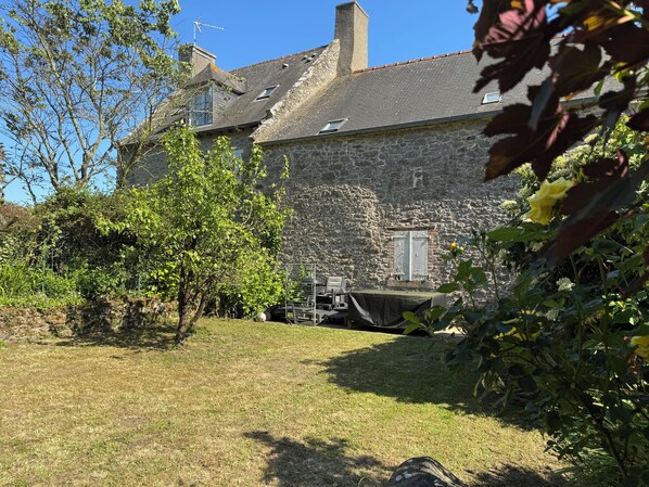 A stone building with a sloped roof, a chimney, and a window with shutters.