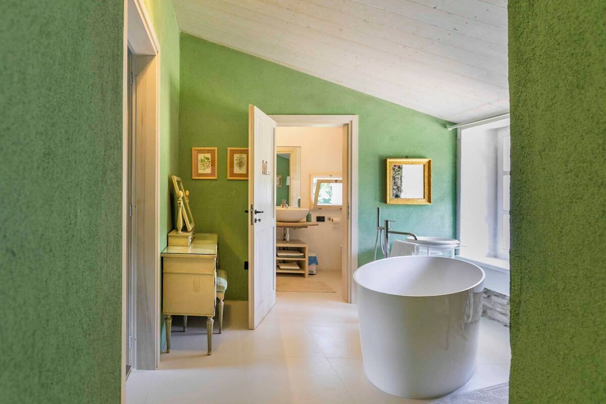 A bathroom with a large bathtub, a sink, and a toilet. There are framed pictures on the wall and a window providing natural light.