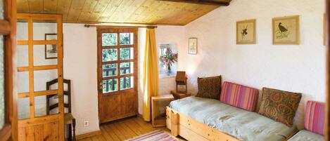 A cozy room with a wooden bed, a wooden chair, a small table, and a window with curtains.