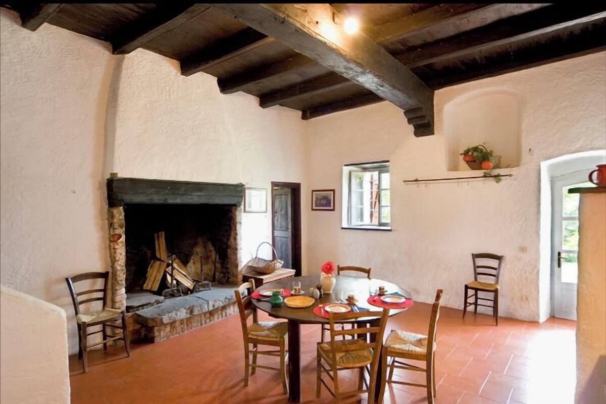 A rustic dining area with a stone fireplace, wooden beams, and a round table set for six.