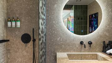 A bathroom with a round mirror, a sink, and three bottles of Bvlgari perfume.