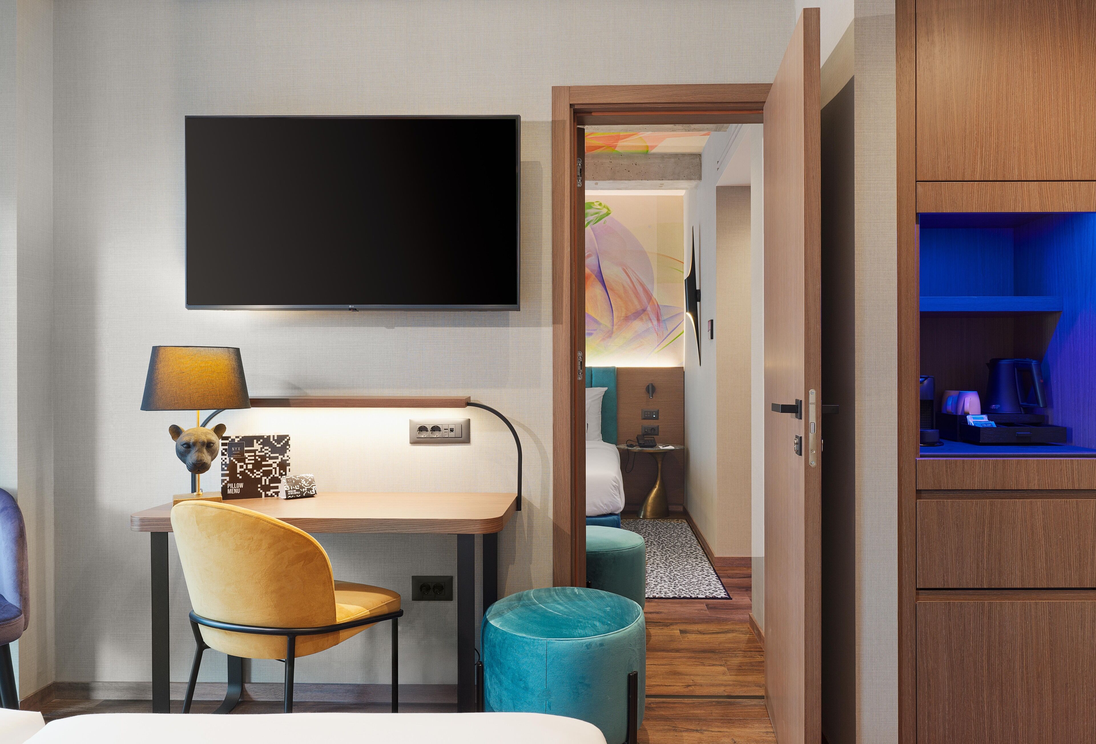 Habitación de hotel con televisor de pantalla plana montado en la pared, un escritorio con lámpara, una silla y una cama.