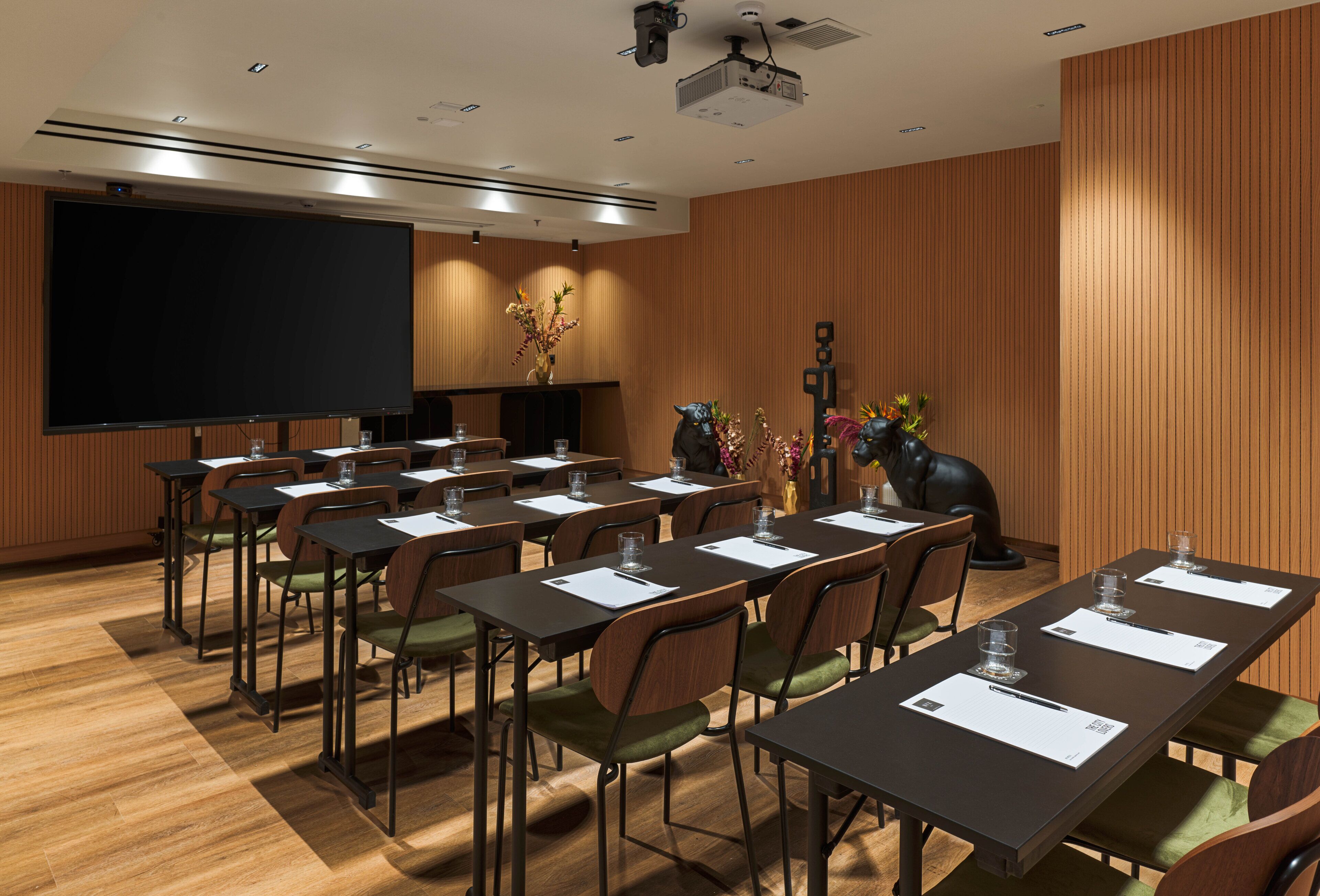 Un salón de conferencias con varias mesas y sillas, una pantalla grande y un proyector.