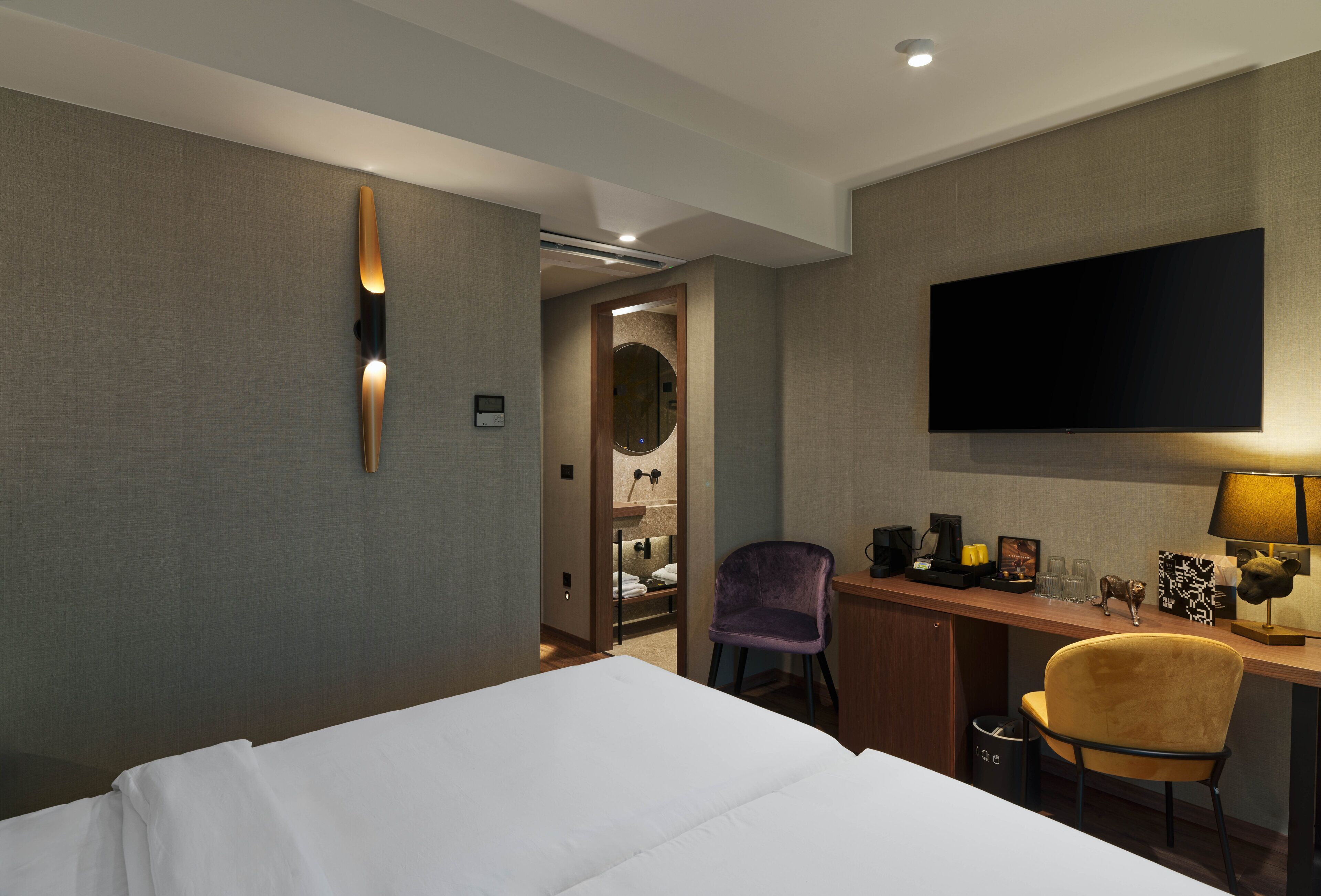 Une chambre d’hôtel comprenant un lit, un bureau avec un téléviseur à écran plat, une chaise et une coiffeuse avec un miroir.