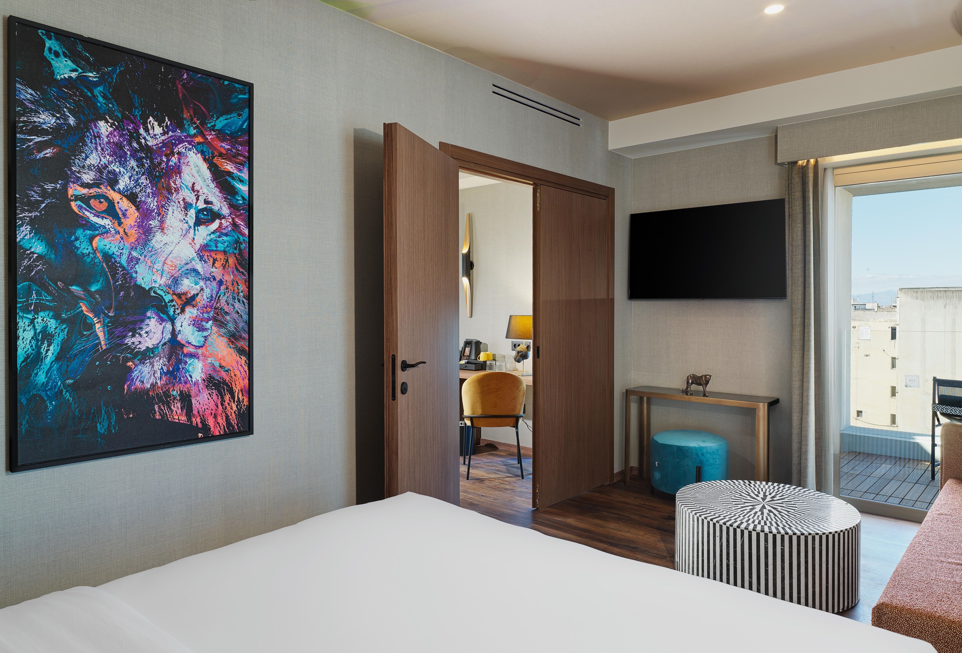 Una camera d'albergo con un'ampia tela astratta, un letto, una scrivania, una sedia e una TV a parete.