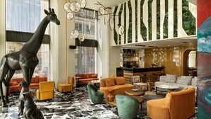 A modern hotel lobby with a large giraffe sculpture, comfortable seating, a bar area, and a view of the city through large windows. - NYX Hotel Thessaloniki (Thessaloniki)