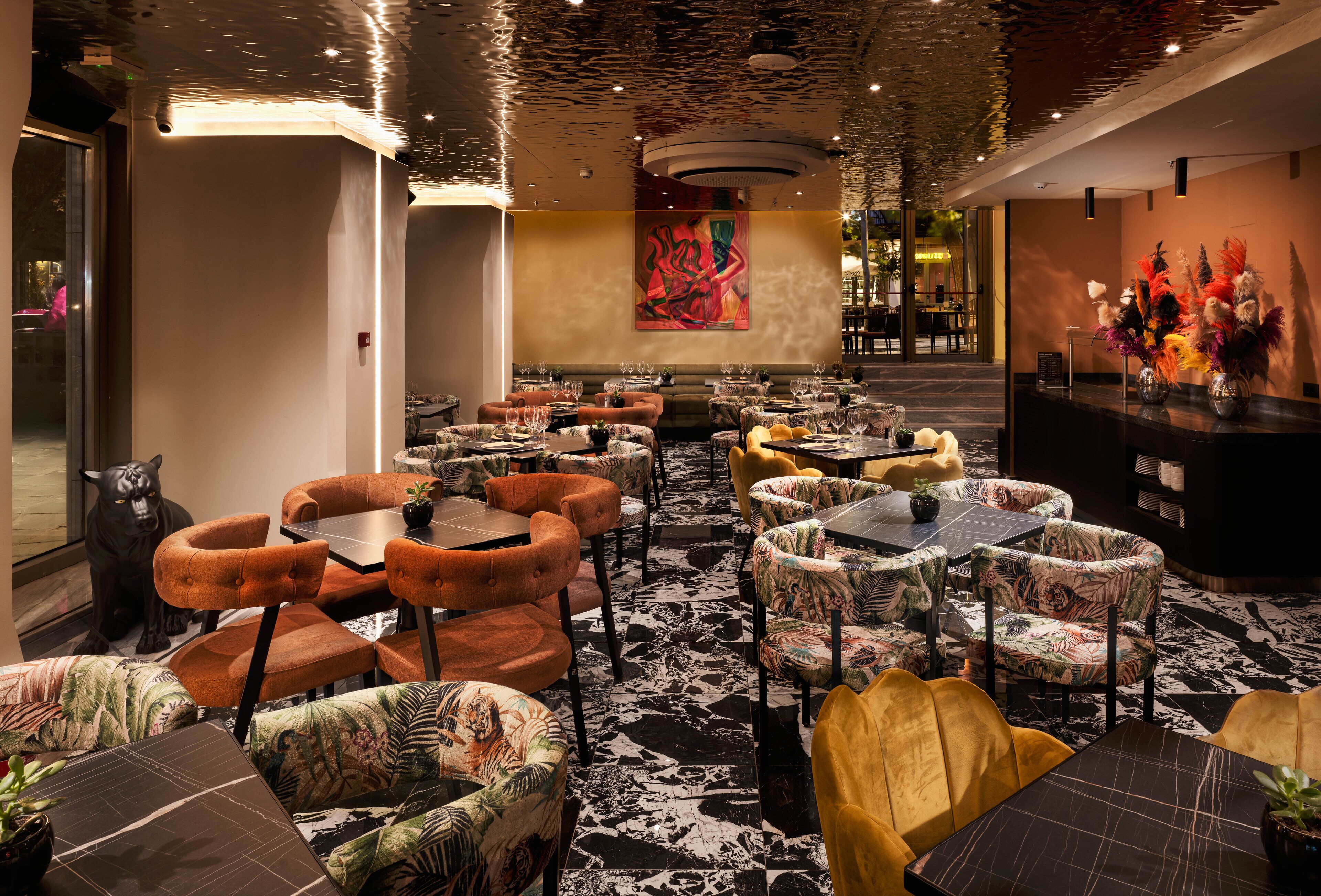 A restaurant with multiple tables and chairs, a black panther statue, and a large abstract painting on the wall.