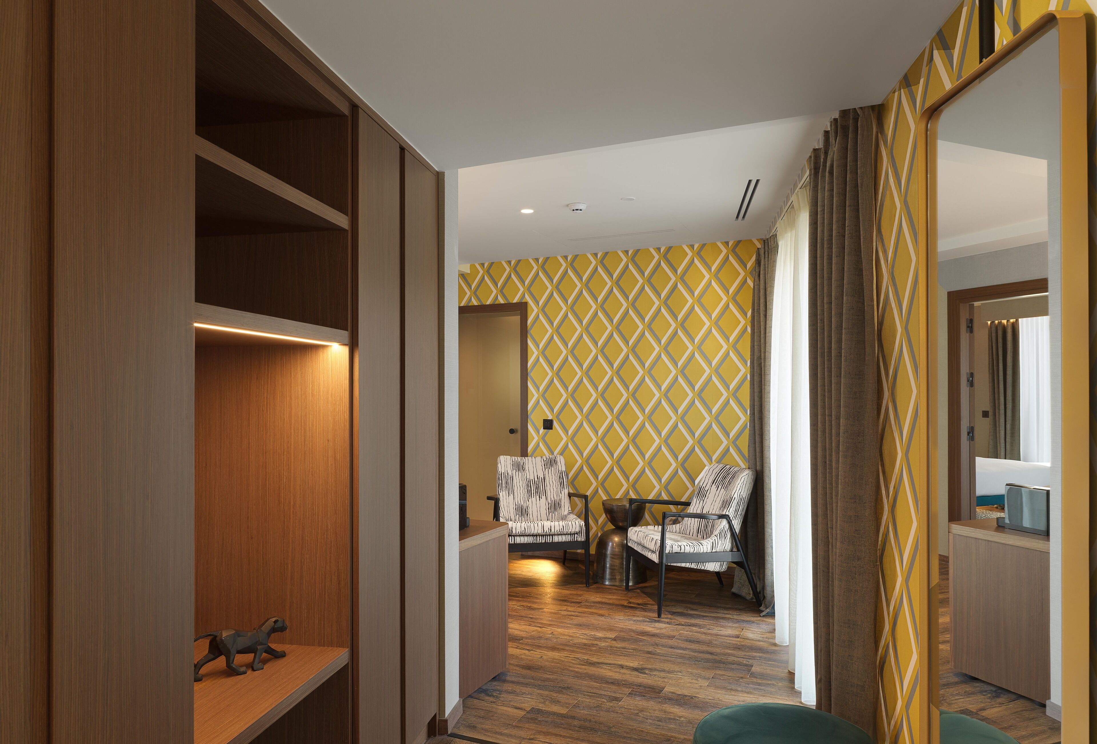 Un pasillo con estanterías de madera, un papel pintado decorativo, dos sillones, una mesita y un televisor.