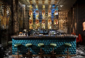 Un espace bar doté d’un comptoir aux motifs bleus et verts, de plusieurs tabourets et d’une variété de bouteilles et de verres disposés sur des étagères.