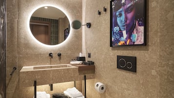 Un baño moderno con un espejo redondo, un lavamanos, un perchero para toallas y un dispensador de papel higiénico.