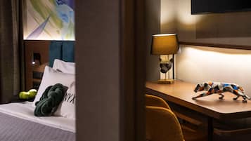 A hotel room with a bed, a desk with a lamp, a chair, and a wall-mounted TV.