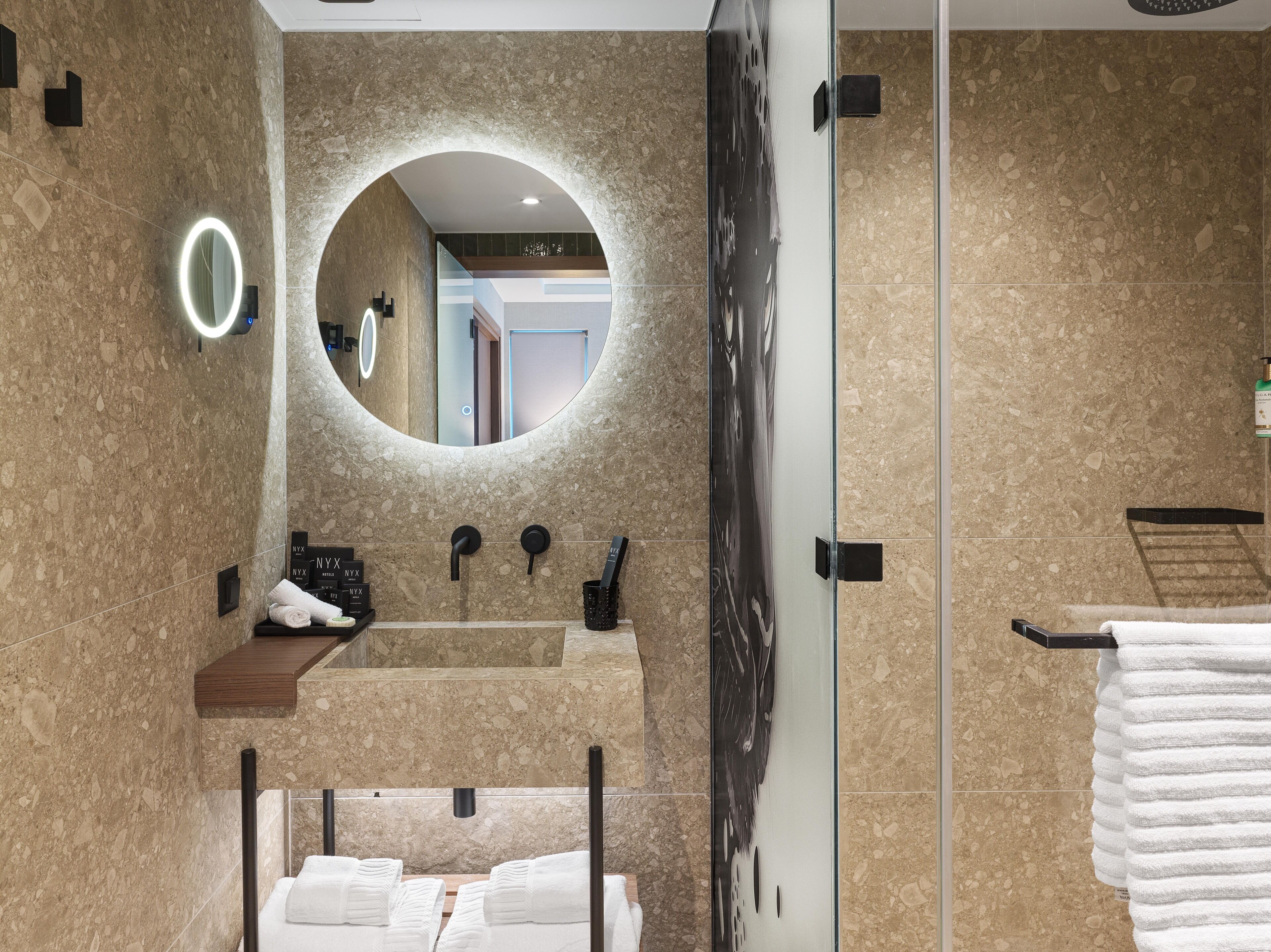 Un baño moderno con un espejo redondo, un lavamanos y una cabina de ducha de vidrio.