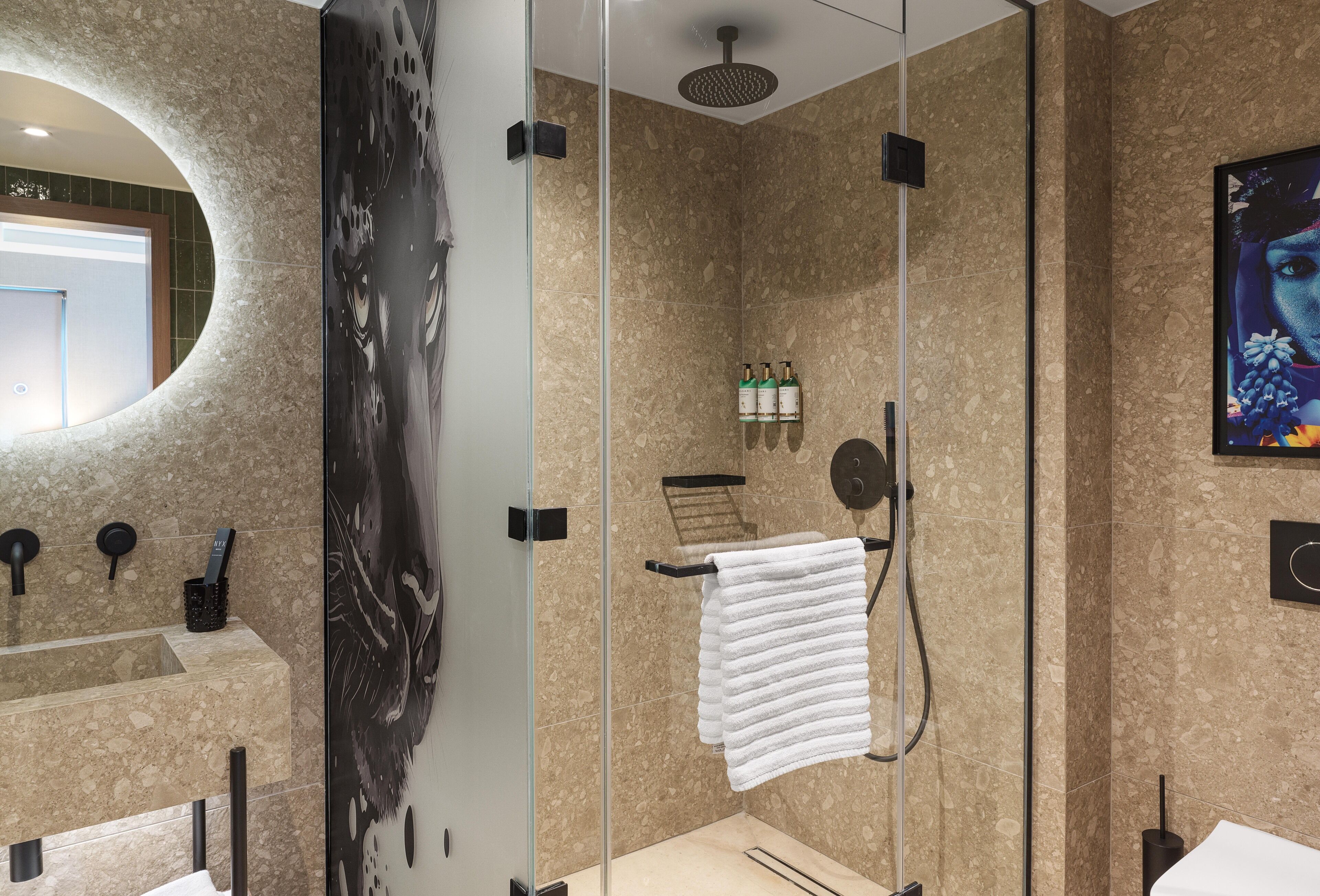 Un baño moderno con ducha de vidrio, lavamanos de mármol y un espejo grande.