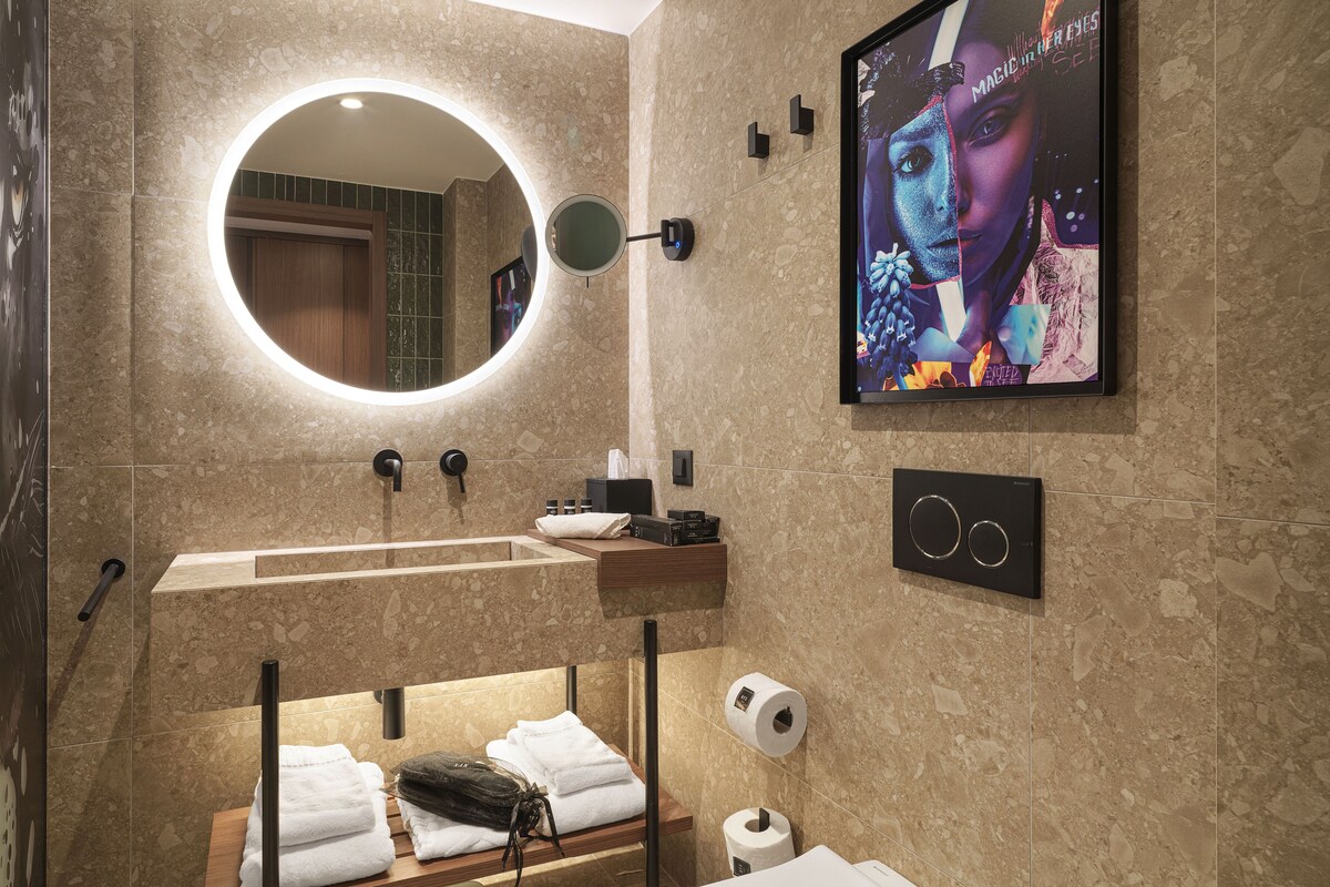 A modern bathroom with a round mirror, a sink, a towel rack, and a toilet paper holder.