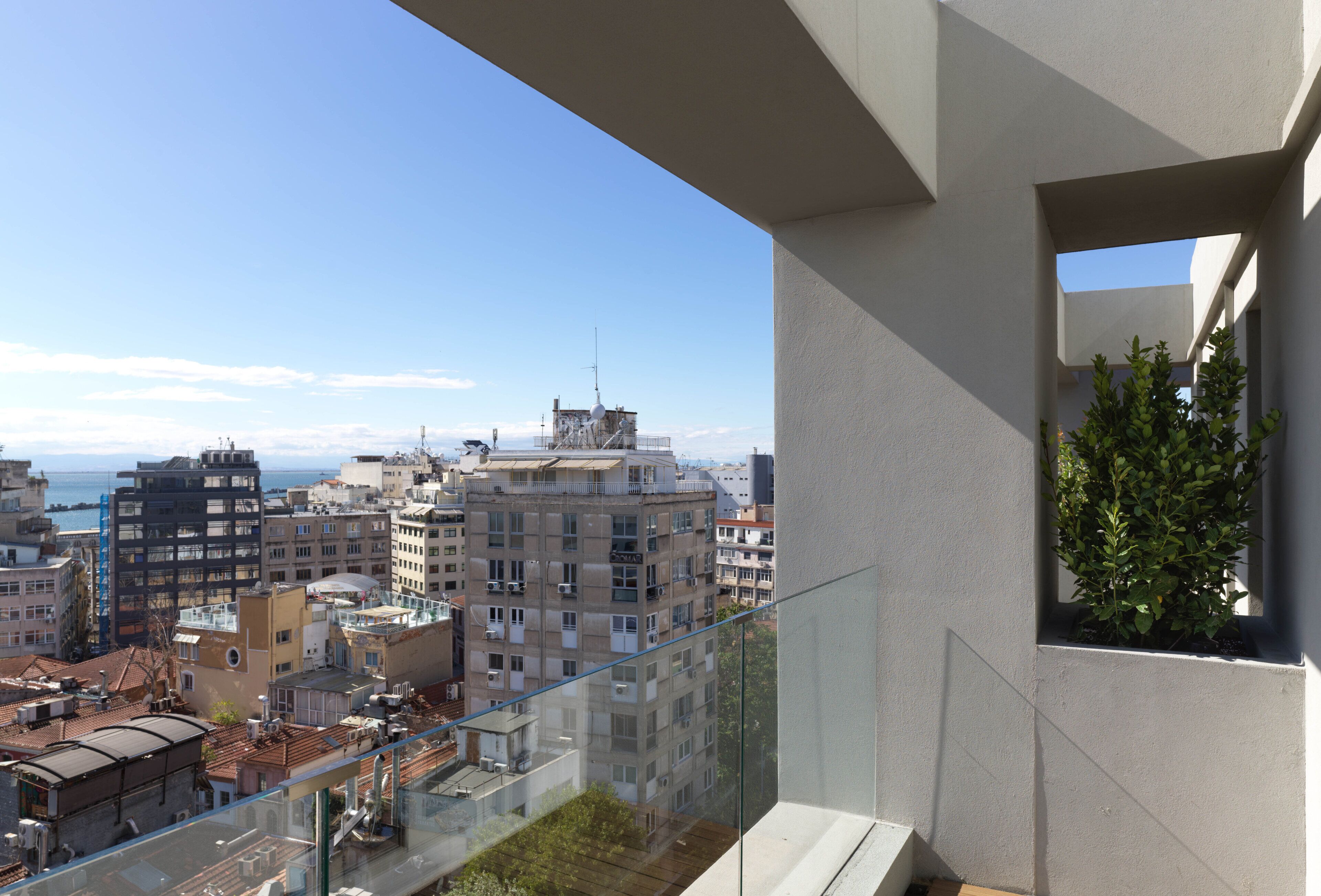 A high-rise building with a balcony overlooking a cityscape and the sea.