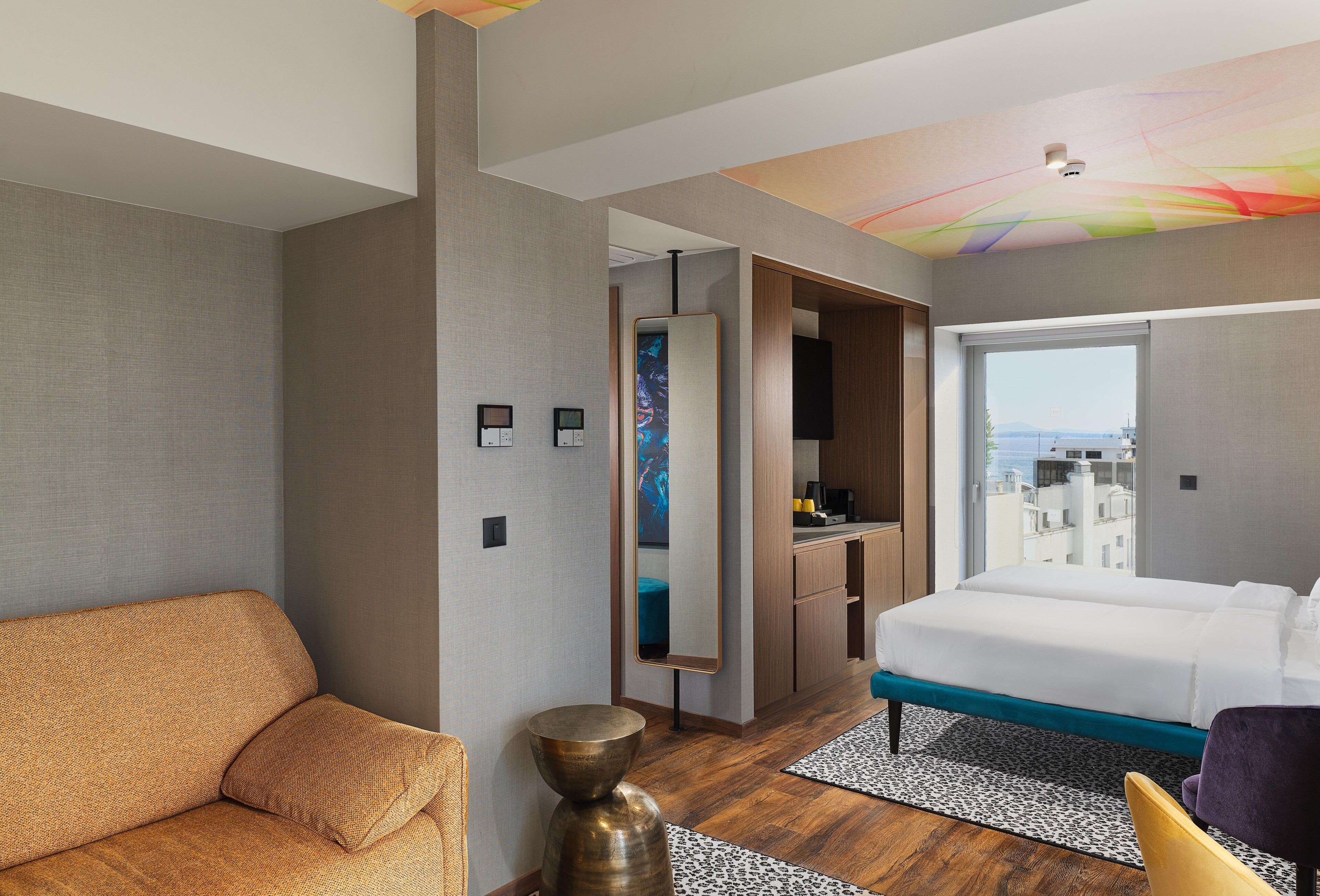 Une chambre d’hôtel moderne avec un canapé, un lit, un miroir et une vue sur la ville.