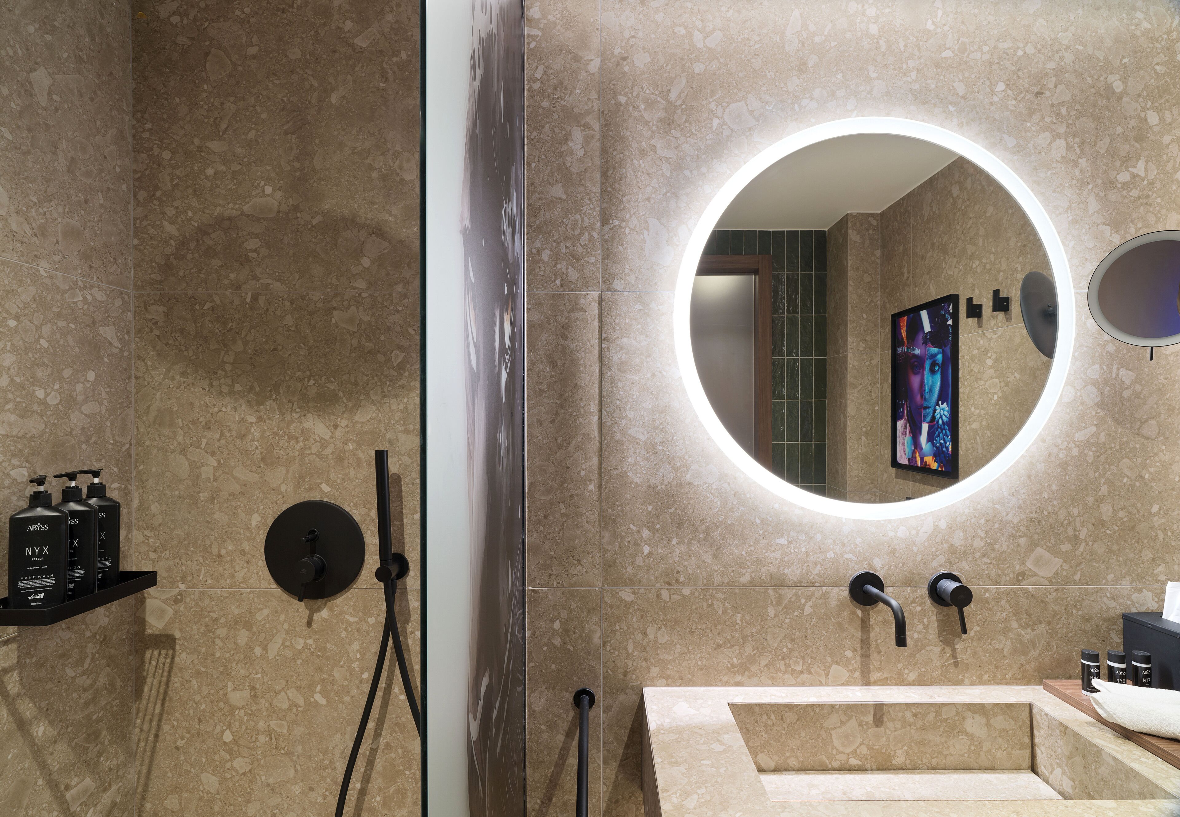 Un baño moderno con un espejo grande, una lámpara redonda y un lavamanos con grifo negro.