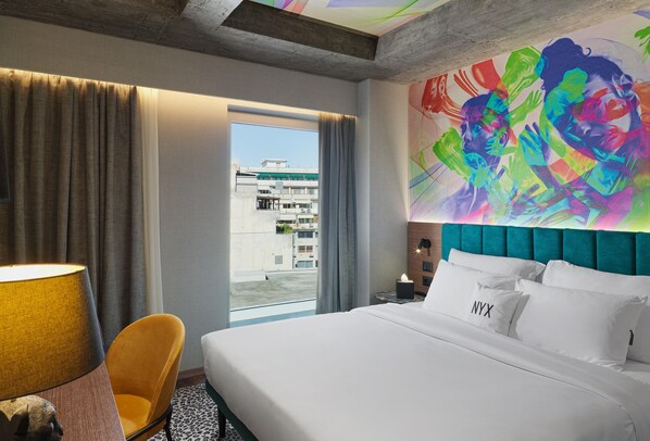 A hotel room with a large bed, a view of the city, and a colorful mural on the wall.