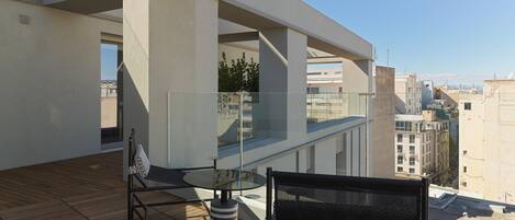 Un balcón moderno con una mesa de vidrio y dos sillas, con vistas a un paisaje urbano.