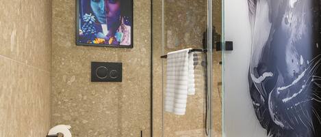 Een moderne badkamer met een glazen douchecabine, toilet en een televisie waarop een kleurrijk beeld wordt weergegeven.