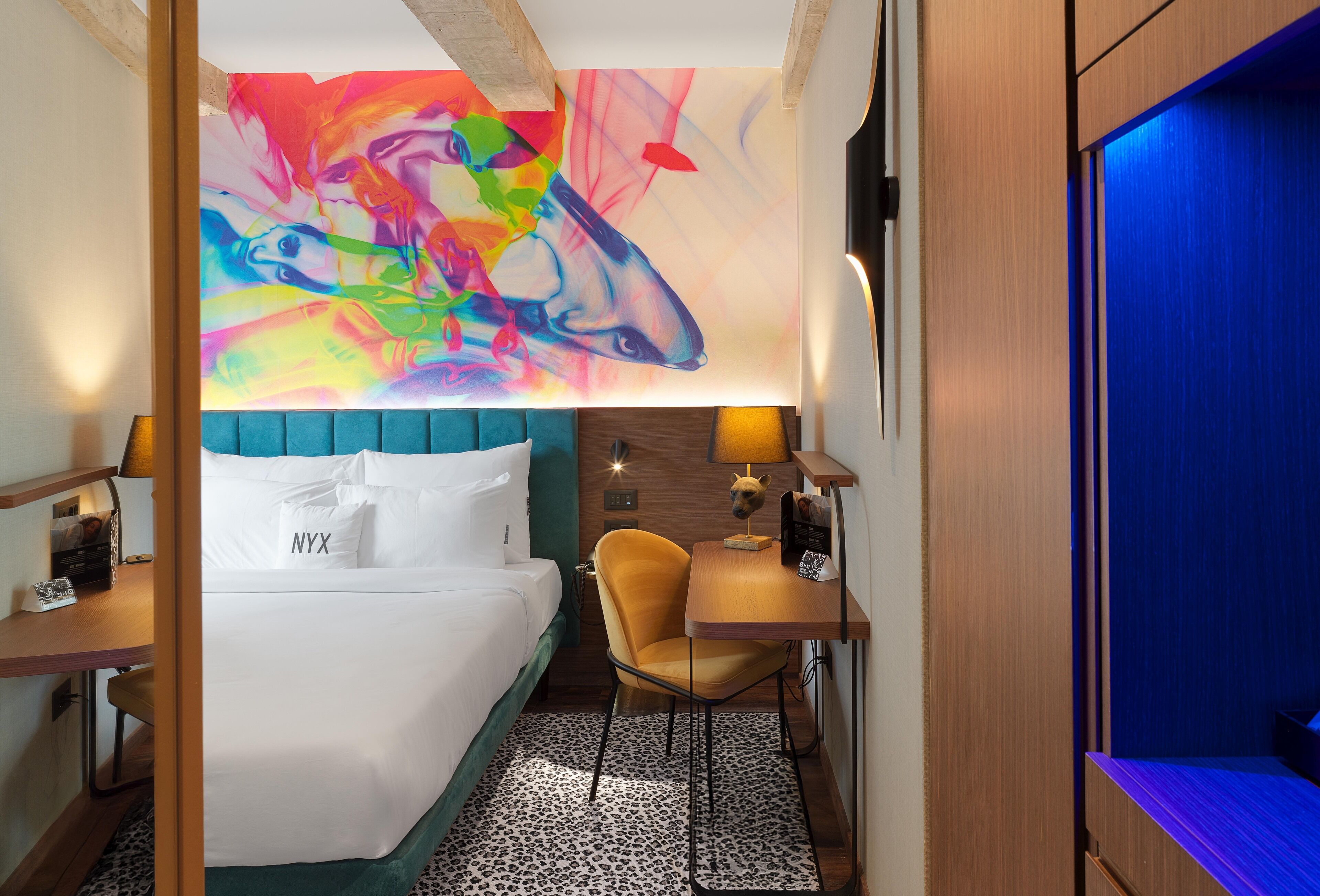 A hotel room with a bed, a desk, and a vibrant abstract painting on the wall.