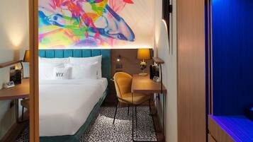 A hotel room with a bed, a desk, and a vibrant abstract painting on the wall.