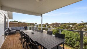 Una terraza techada al aire libre con una mesa y sillas para comer, un sofá y vistas del paisaje circundante.