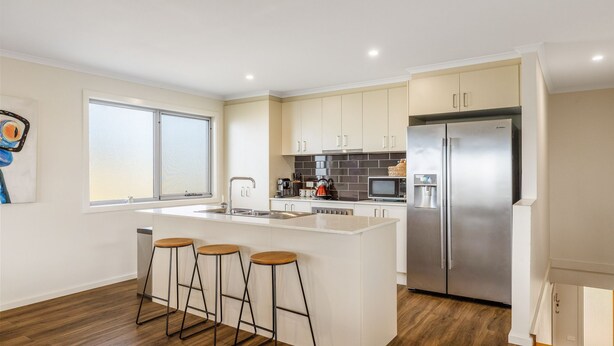 Una cocina moderna con una isla central, electrodomésticos de acero inoxidable y taburetes de madera.