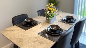 Une table à manger dressée avec de l’argenterie noire, des couverts et des verres à vin, agrémentée d’un centre de table floral et offrant une vue sur la verdure à l’extérieur.