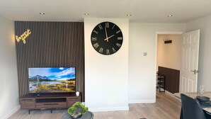 Un salon moderne doté d’un téléviseur à écran plat, d’une grande horloge murale et d’un mur recouvert de panneaux en bois.