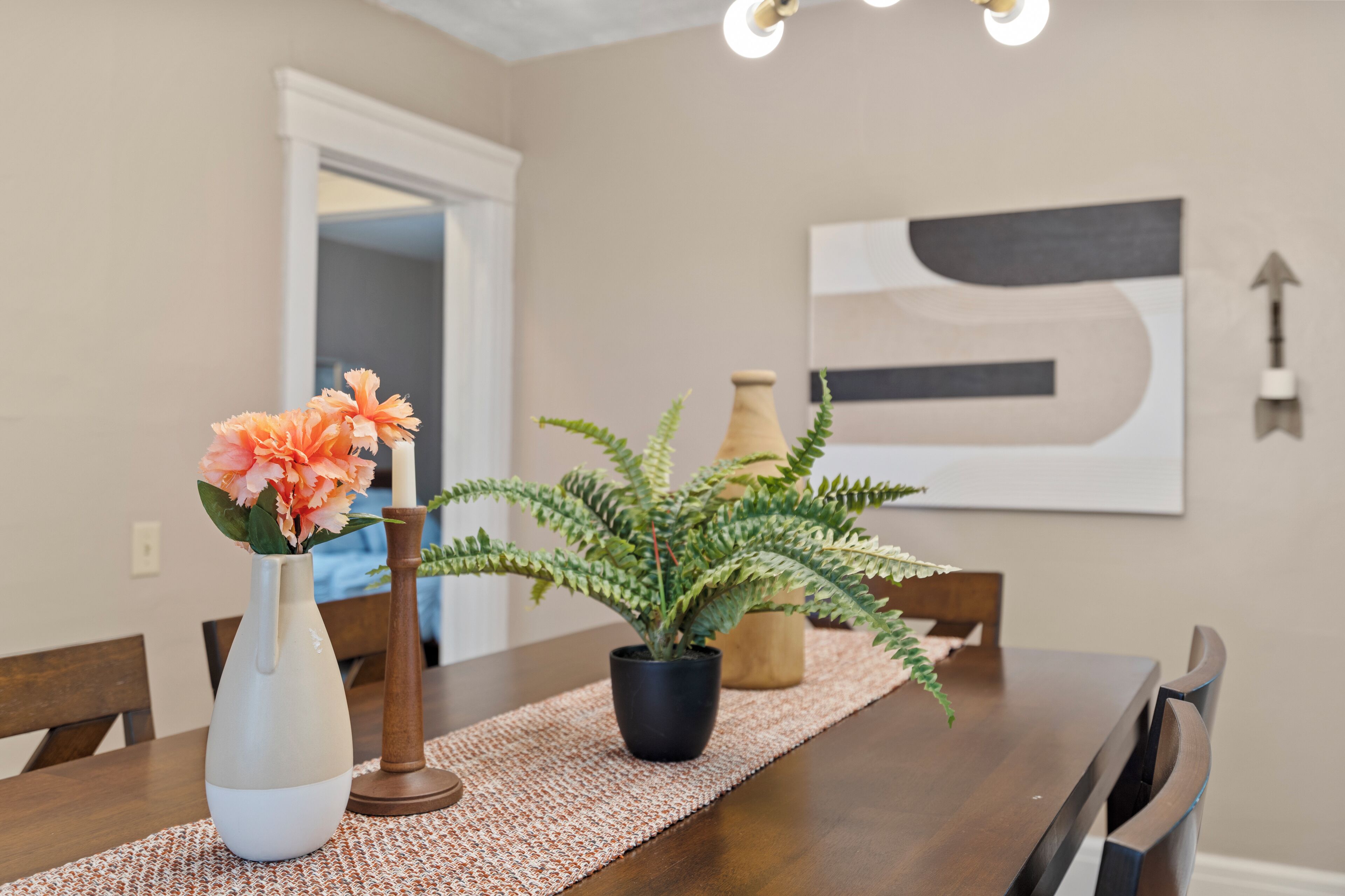 A dining table with a vase of flowers, a potted plant, and a textured placemat.