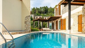 A swimming pool with a stone wall and wooden shutters, surrounded by a building with balconies and a stone facade.