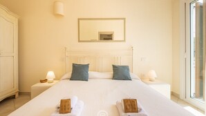 A hotel room with a large bed, two pillows, a nightstand with a lamp, a mirror on the wall, and a window with a view.
