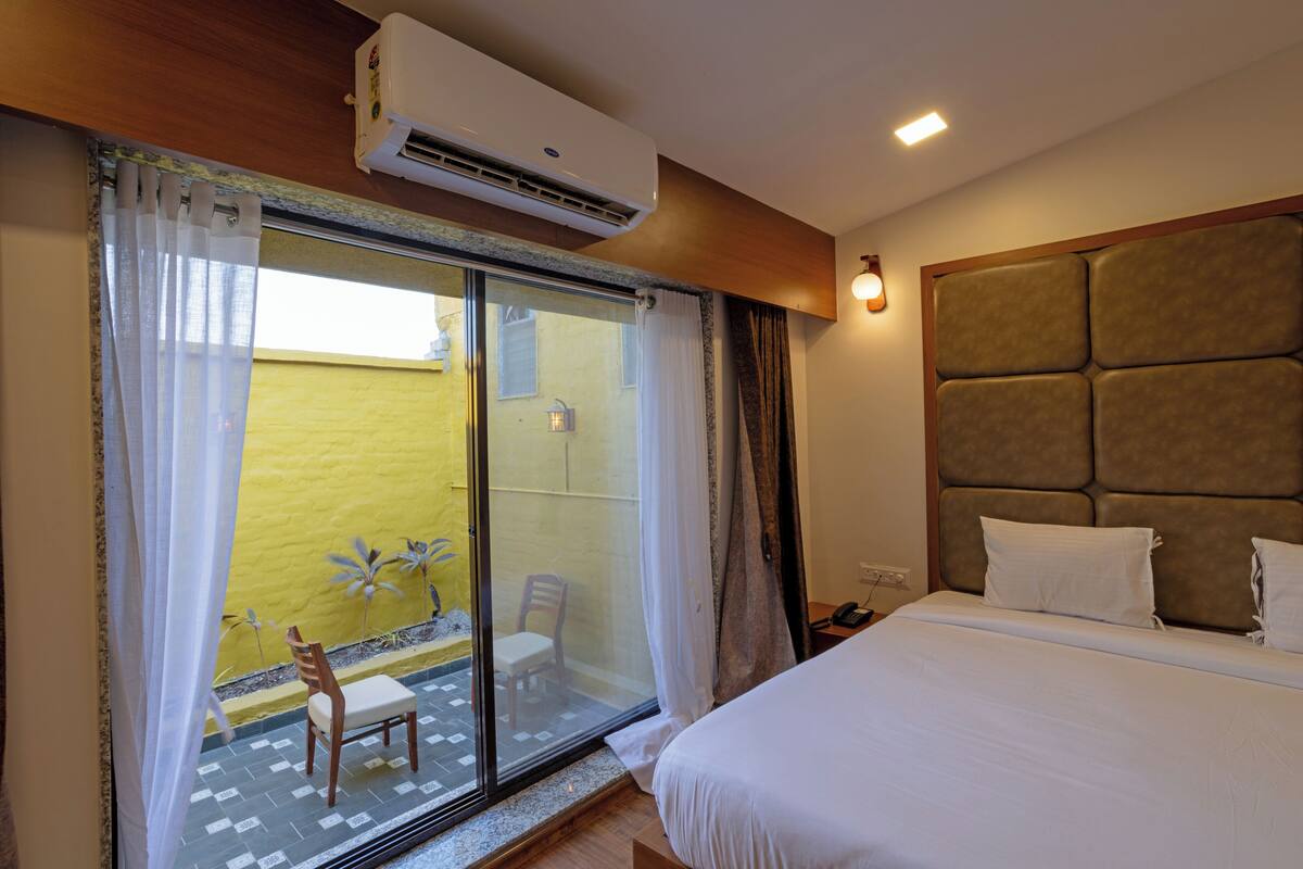 Habitación de hotel con cama, puerta corrediza de vidrio a un balcón, una silla y un equipo de aire acondicionado.