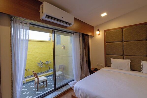Habitación de hotel con cama, puerta corrediza de vidrio a un balcón, una silla y un equipo de aire acondicionado.