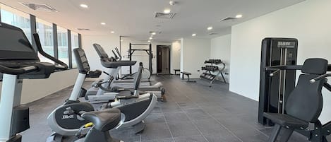 A modern gym with various cardio machines, weightlifting equipment, and a bench.