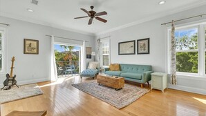A spacious living room with hardwood flooring, a teal sofa, a wooden coffee table, and a ceiling fan.