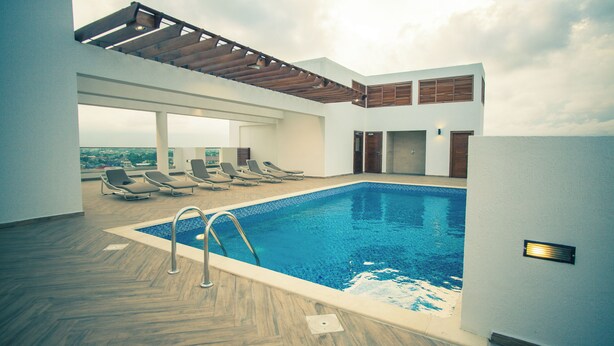 Una piscina interior con terraza de madera, sillones de descanso y vistas a la ciudad.