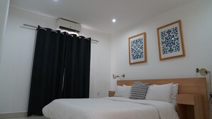Una habitación de hotel con una cama, una cortina negra, dos obras de arte decorativas en la pared y un equipo de aire acondicionado.