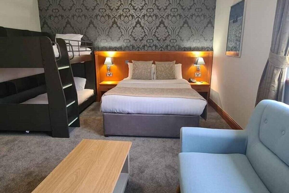 Habitación de hotel con literas, cama individual, sofá y una pequeña mesa, además de un papel tapiz estampado.
