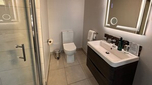 Un bany modern amb boxa de dutxa de vidre, un vàter blanc i un lavabo amb mirall.