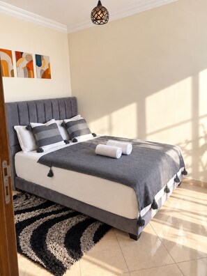 A modern bedroom with a grey upholstered bed, a patterned throw, and a black and white rug.