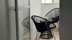 A balcony with two black wireframe chairs, a white towel, and a potted plant with flowers.