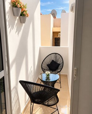A balcony with two black chairs, a small table, and potted plants.